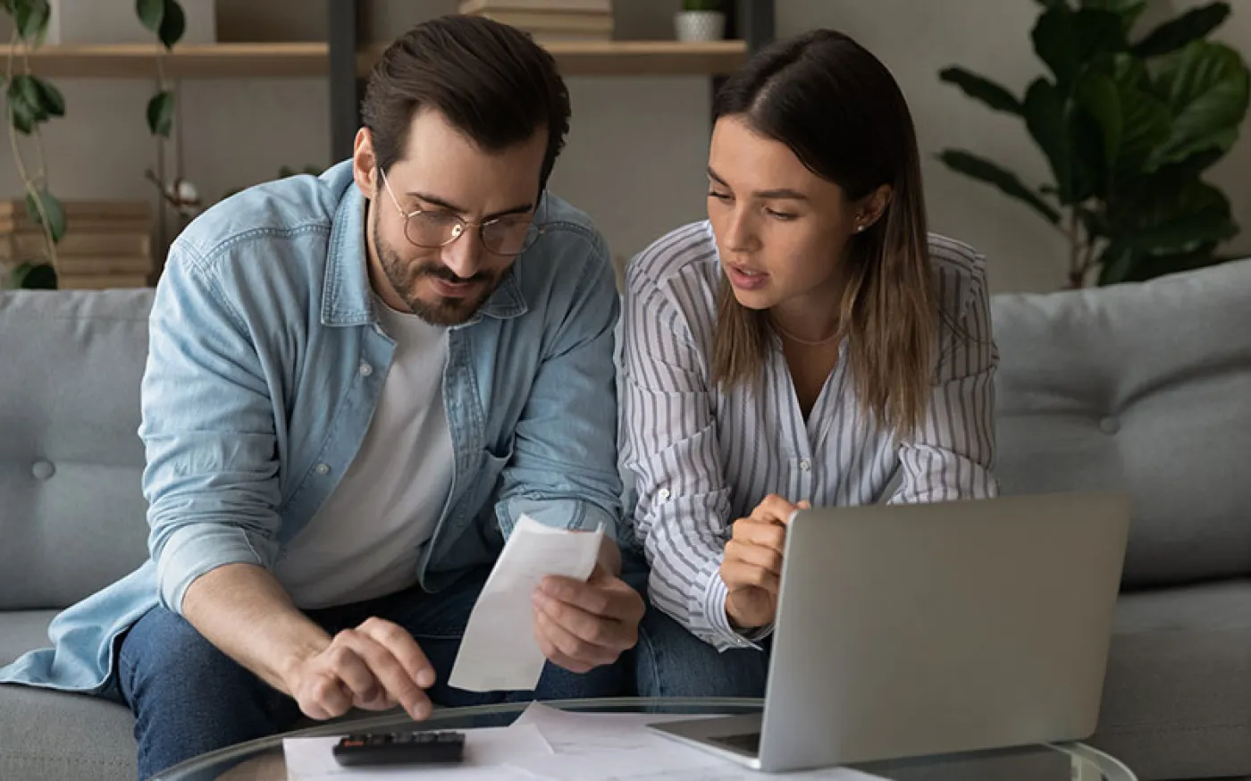 A couple sitting on a couch working on a laptop together.